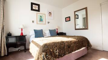 Une chambre à coucher comprenant un lit, deux tables de chevet, un miroir et des œuvres d’art murales.
