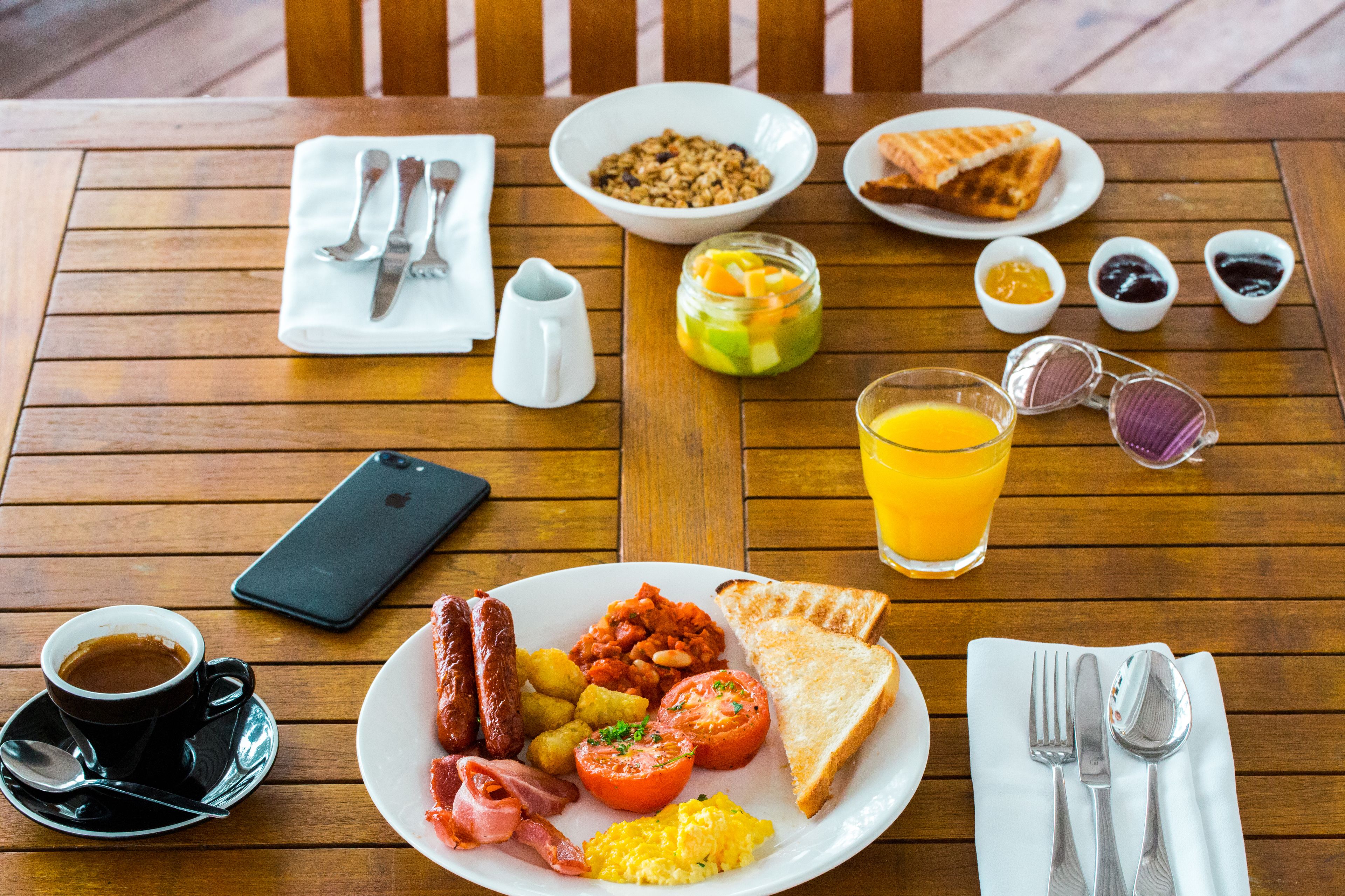 Una mesa de madera con alimentos para el desayuno, incluyendo tostadas, salchichas, huevos y un vaso de zumo de naranja.