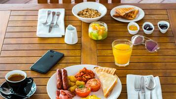 Una mesa de madera con alimentos para el desayuno, incluyendo tostadas, salchichas, huevos y un vaso de zumo de naranja.