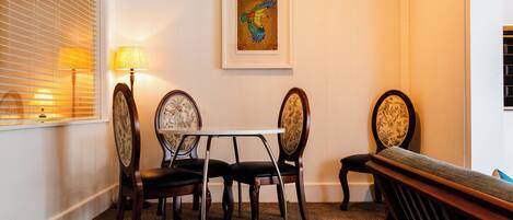 Un comedor con una mesa y cuatro sillas, una obra de arte enmarcada en la pared y una ventana con persianas.