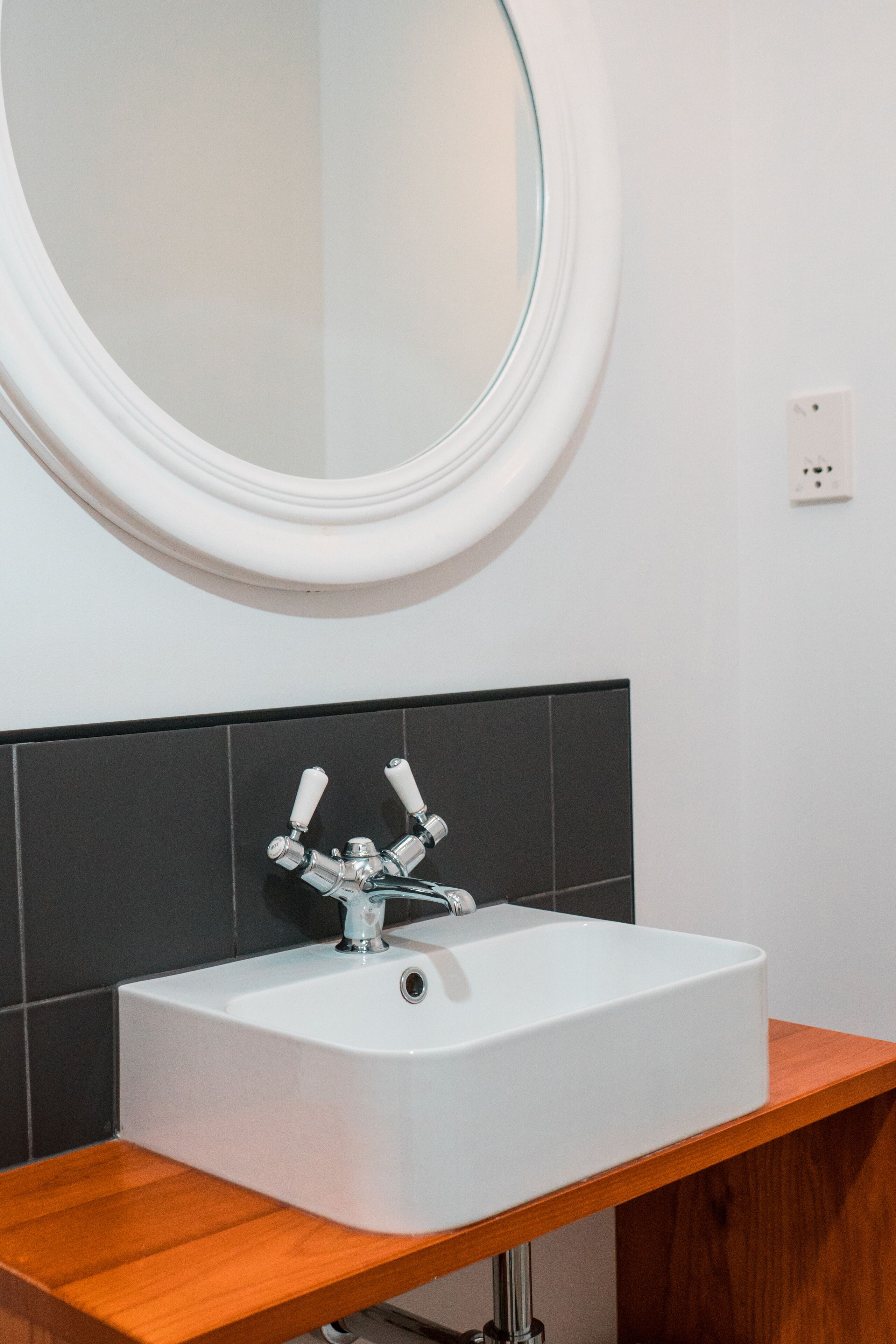Une salle de bain avec un lavabo blanc, un miroir rond et un plan de toilette en bois.