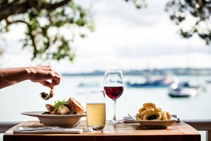 A table with seafood dishes, a glass of red wine, and a view of the sea and boats. - The Duke of Marlborough Hotel (Russell)