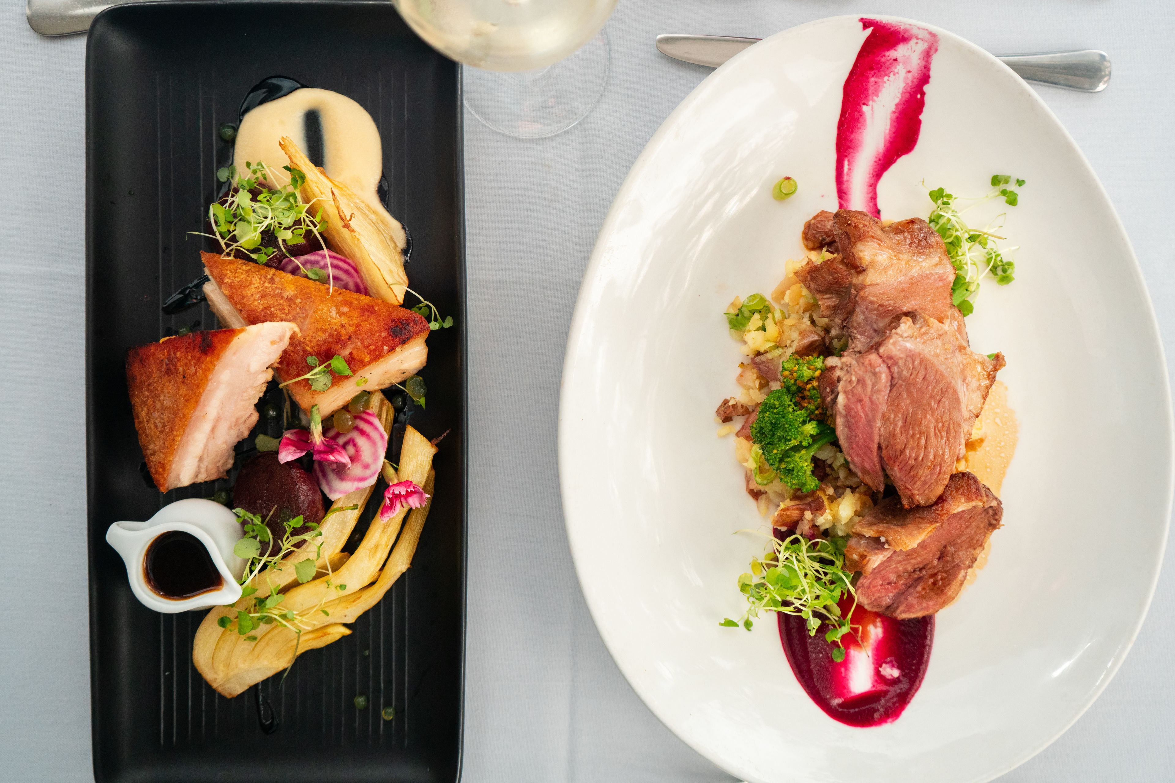 Two plates of food with a glass of white wine.
