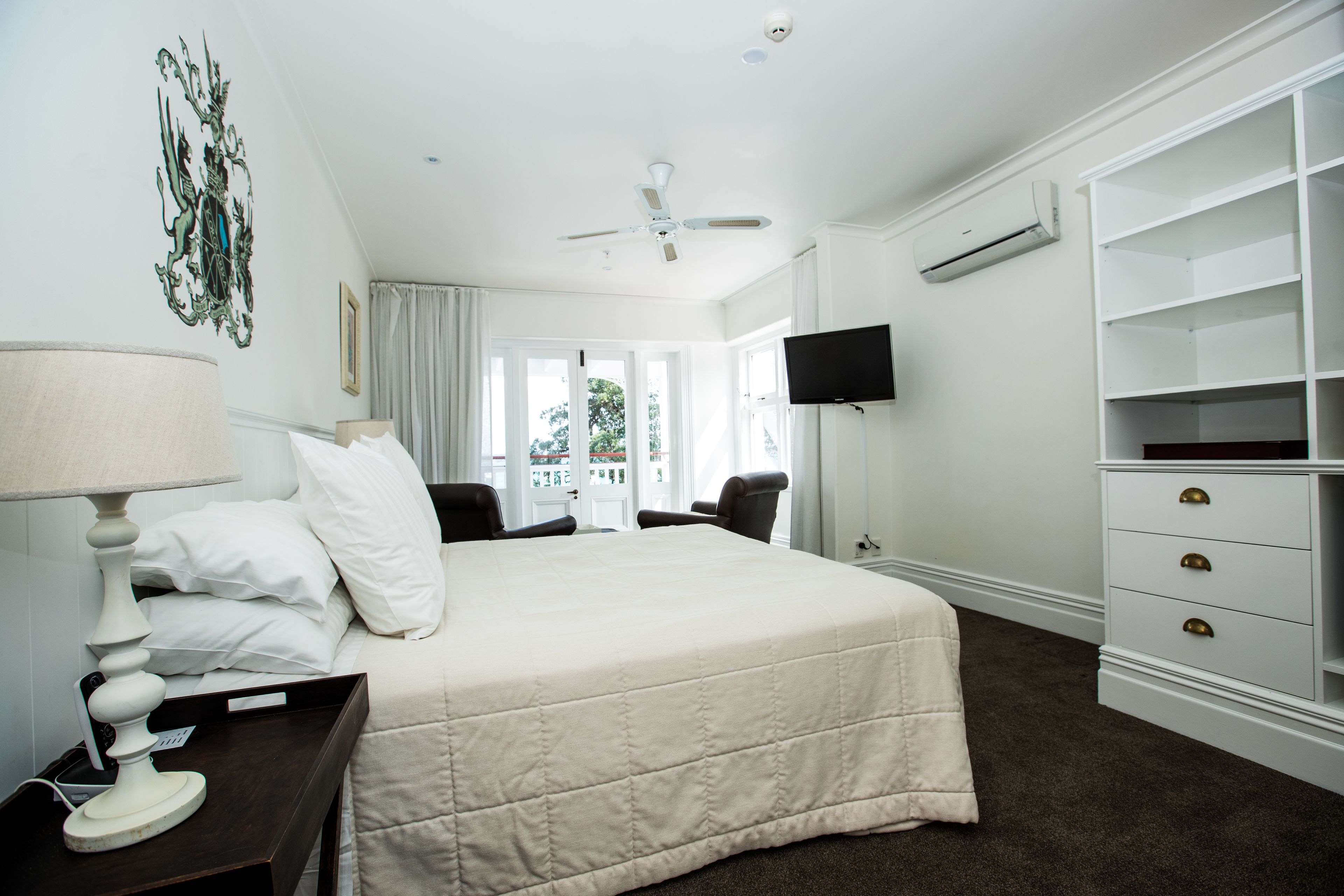A hotel room with a bed, a nightstand, a TV, a wardrobe, and a ceiling fan.
