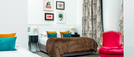 A modern bedroom with a large bed, a red armchair, and a wall with framed artwork.