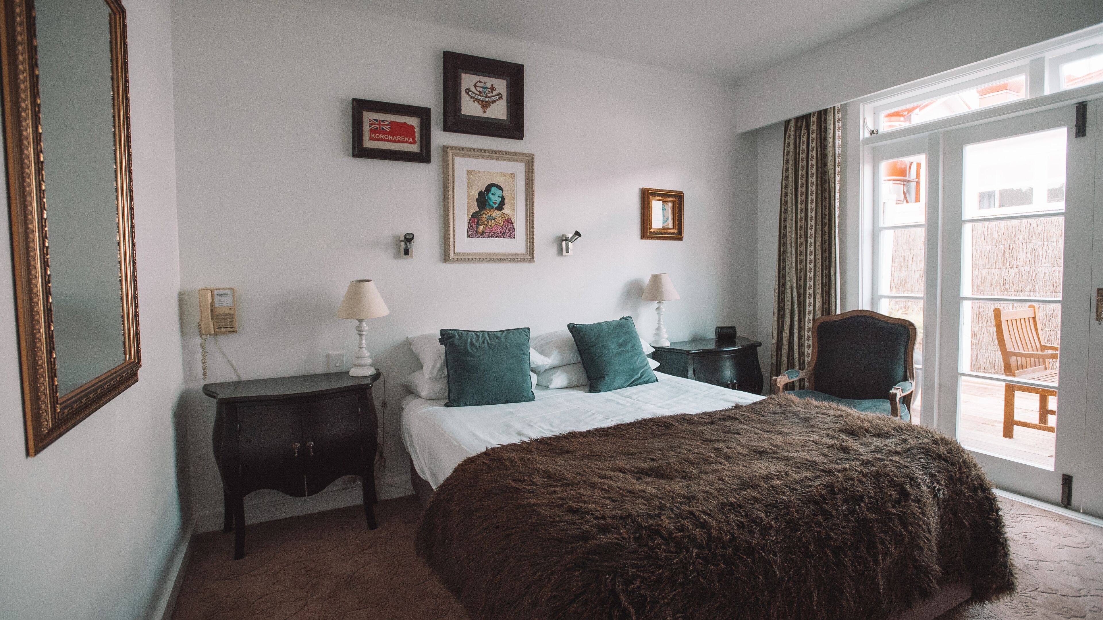 Quarto com uma cama grande, duas mesas de cabeceira com luminárias, uma cadeira e vista para o exterior através de uma porta de correr.