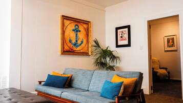 A living room with a blue sofa, two cushions, a framed anchor artwork, and a potted plant.