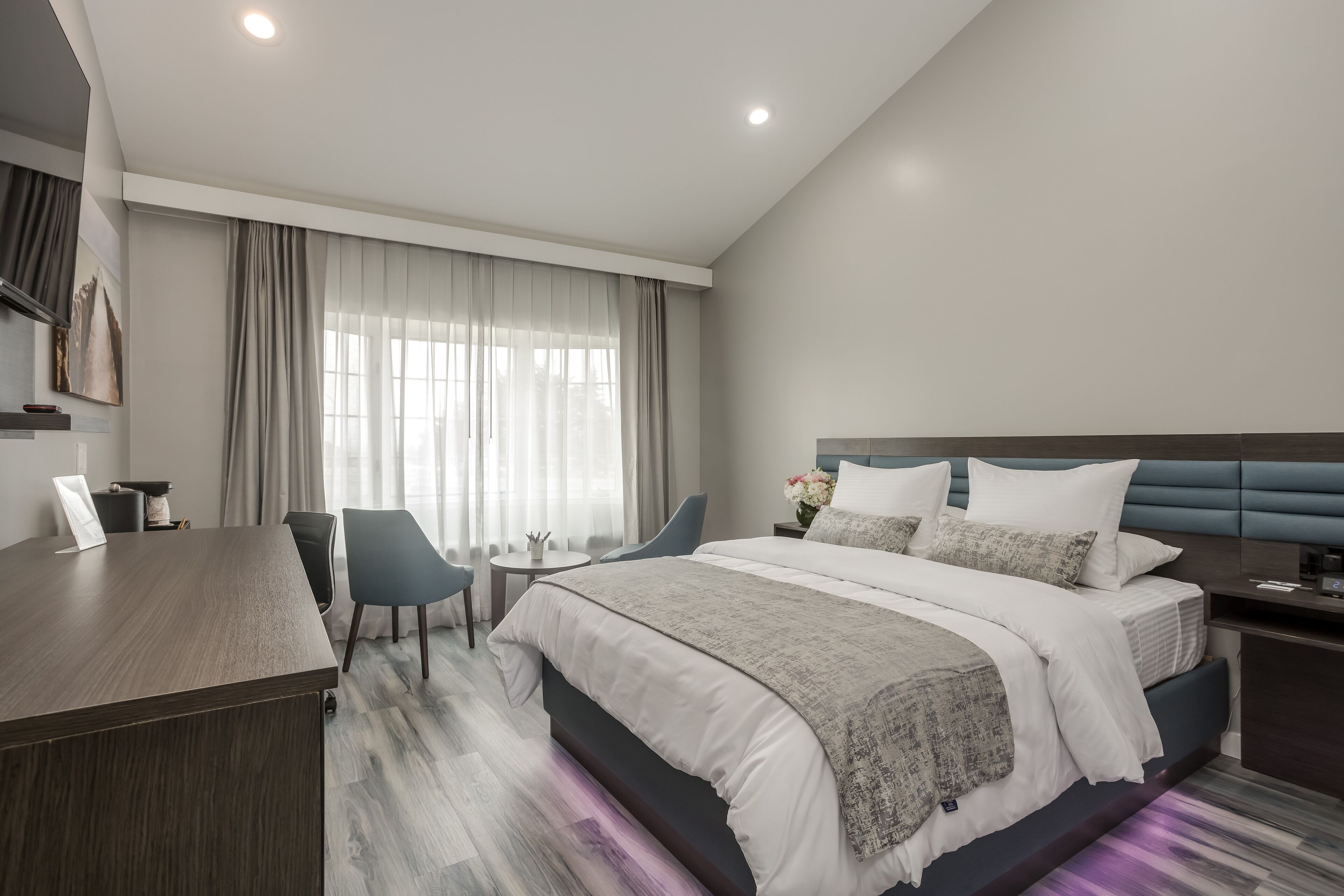 A modern hotel room with a large bed, a desk, and a chair.