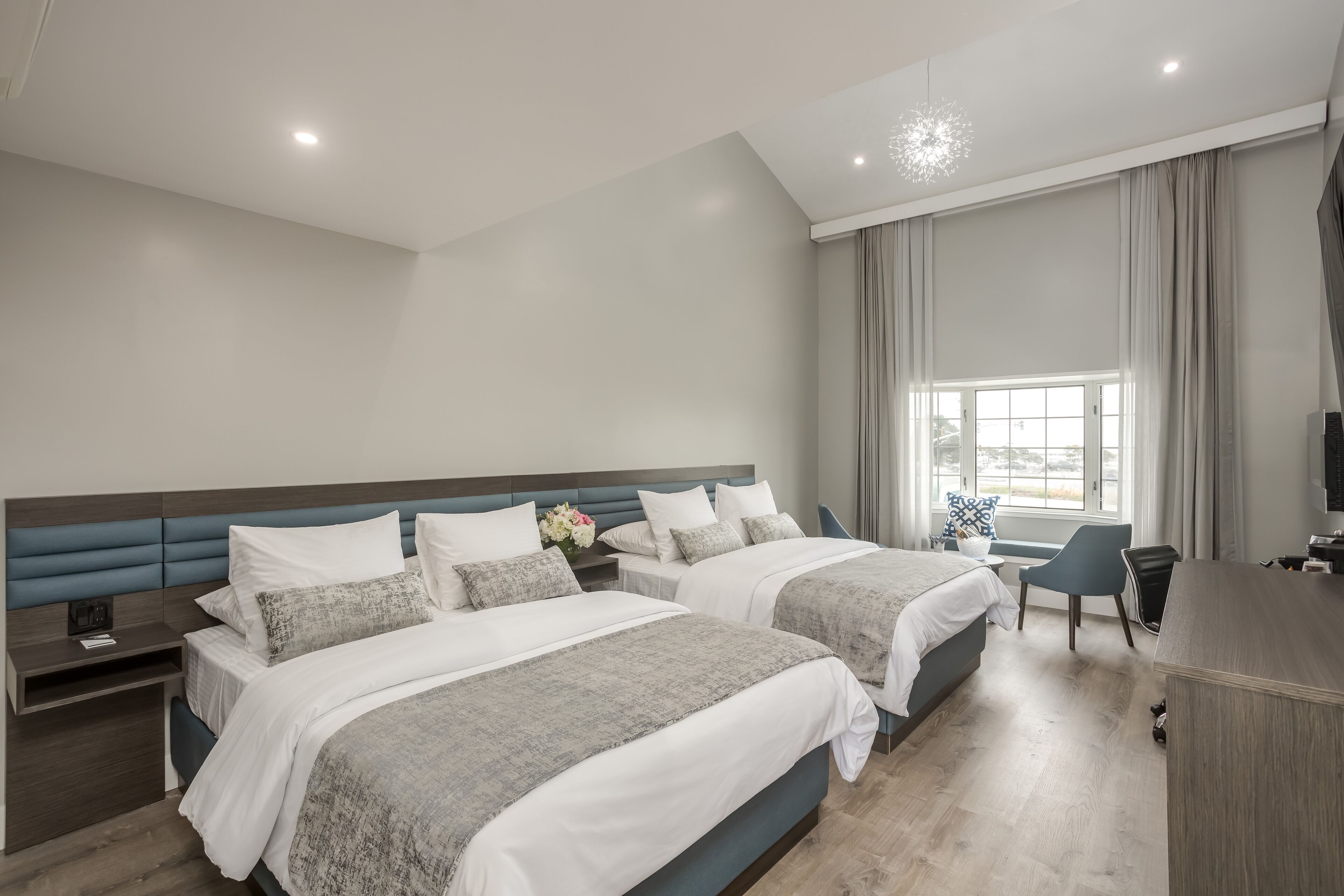 A modern hotel room with two beds, a desk, and a large window with curtains.