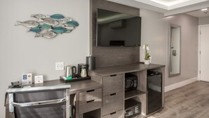 A modern hotel room with a wooden desk, a flat-screen TV, a microwave, and a coffee maker.