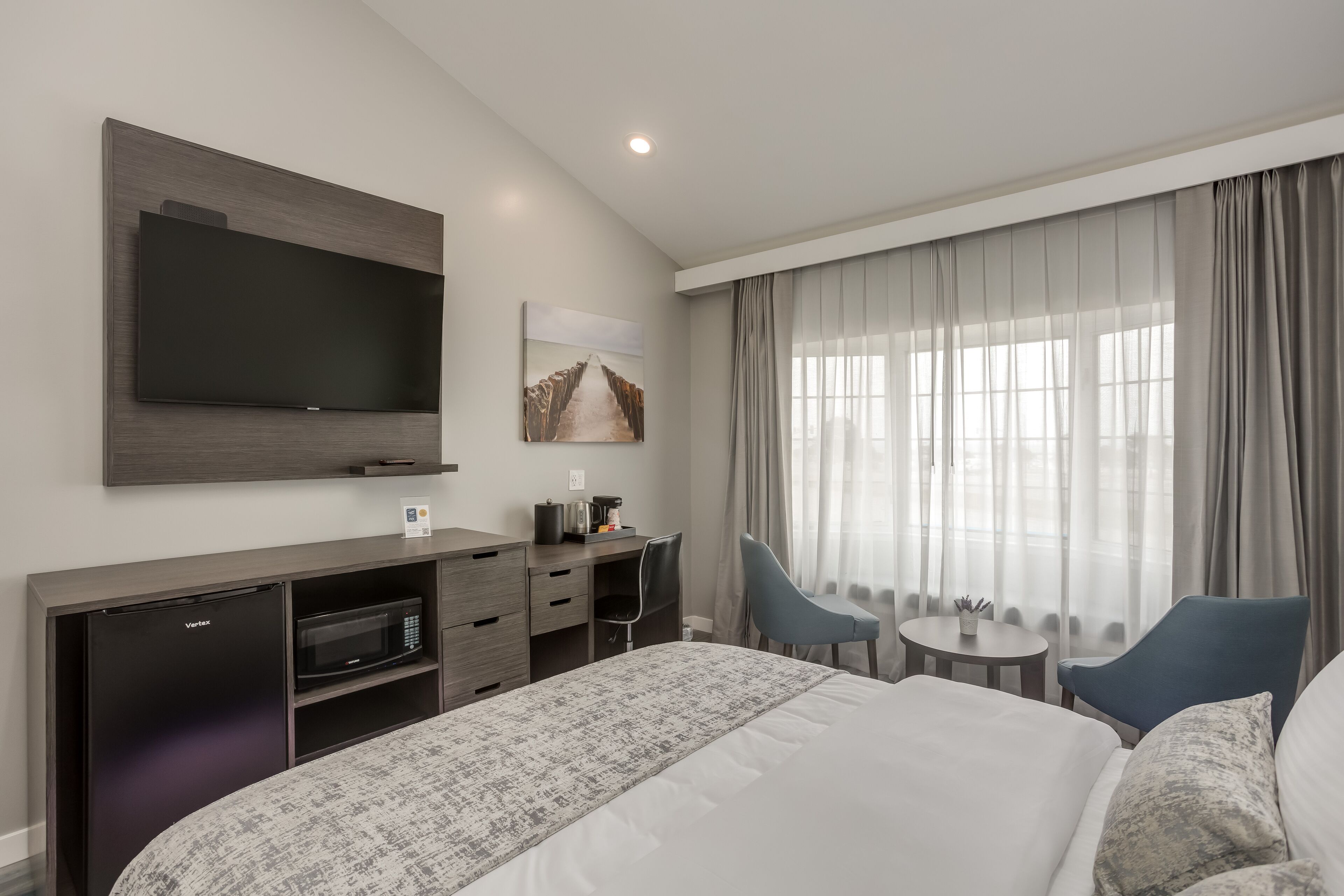 A hotel room with a large bed, a desk with a flat-screen TV, a minibar, and a seating area with a table and chairs.
