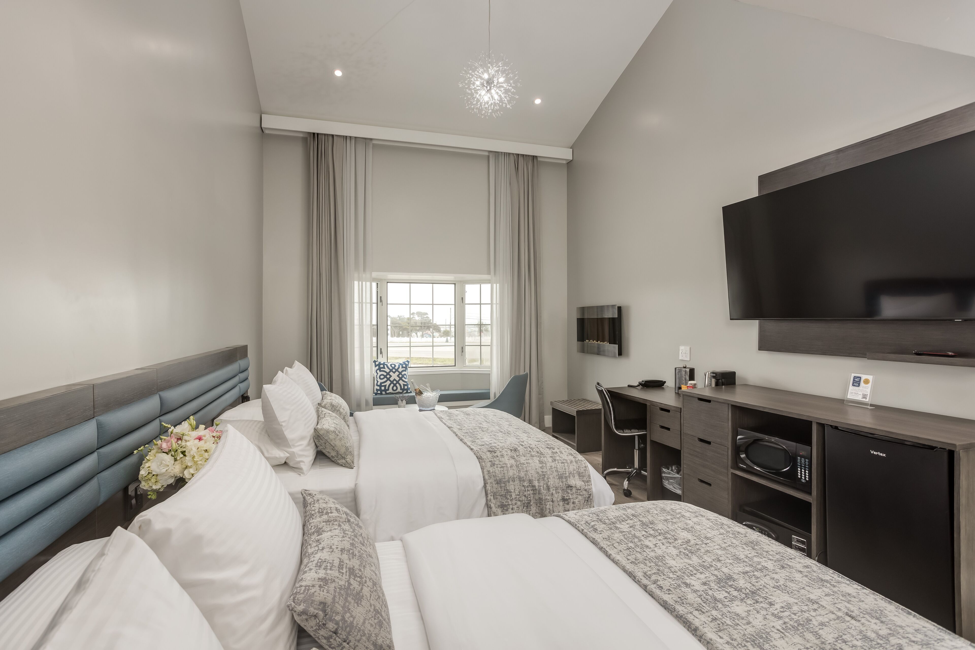 A hotel room with two beds, a desk, a flat-screen TV, a microwave, and a minibar.