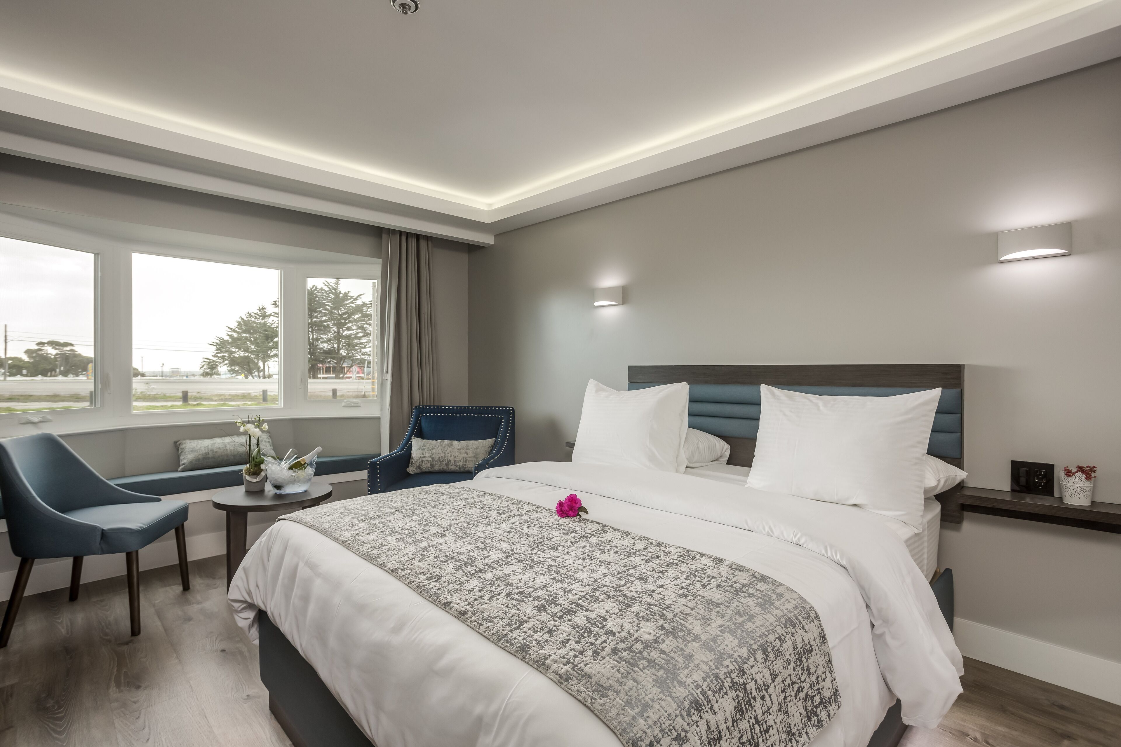 Habitación de hotel con una cama grande, un área de descanso con una silla, una mesita y una ventana con vistas al exterior.