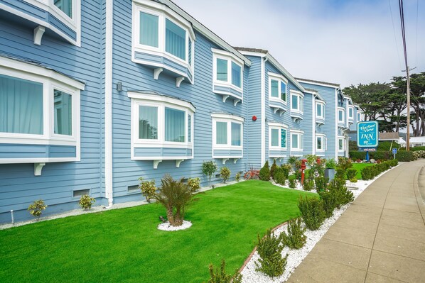 A blue building with white trim, a sign for Harbor View Inn, and a well-maintained lawn with small shrubs.