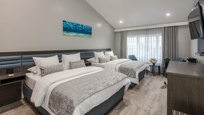 A modern hotel room with two beds, a desk, a TV, and a painting of the ocean on the wall.