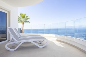 Ein Balkon mit zwei Lounge-Sesseln, einer Palme und Blick aufs Meer.