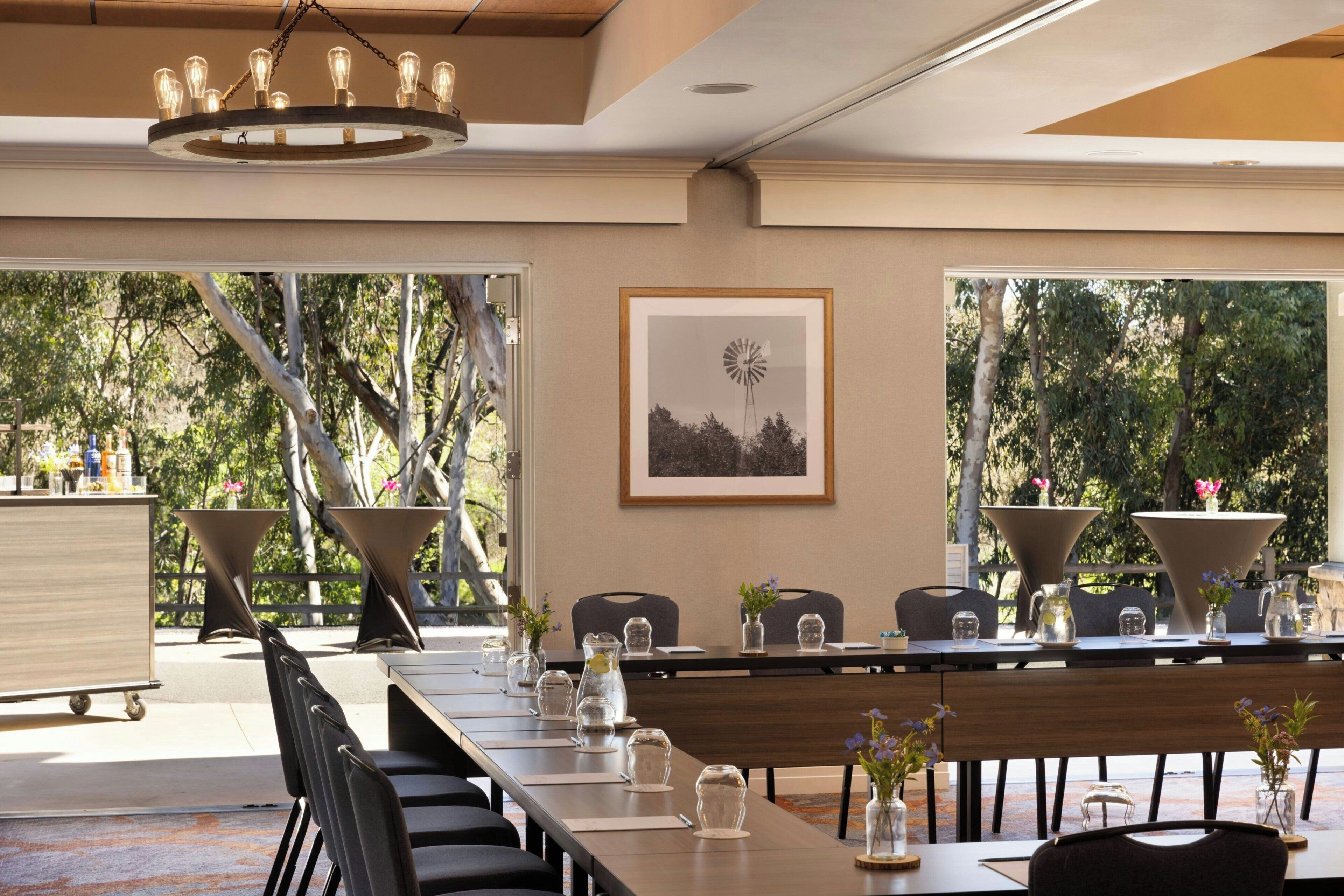 A dining area with a long table, chairs, a chandelier, and a framed picture on the wall.