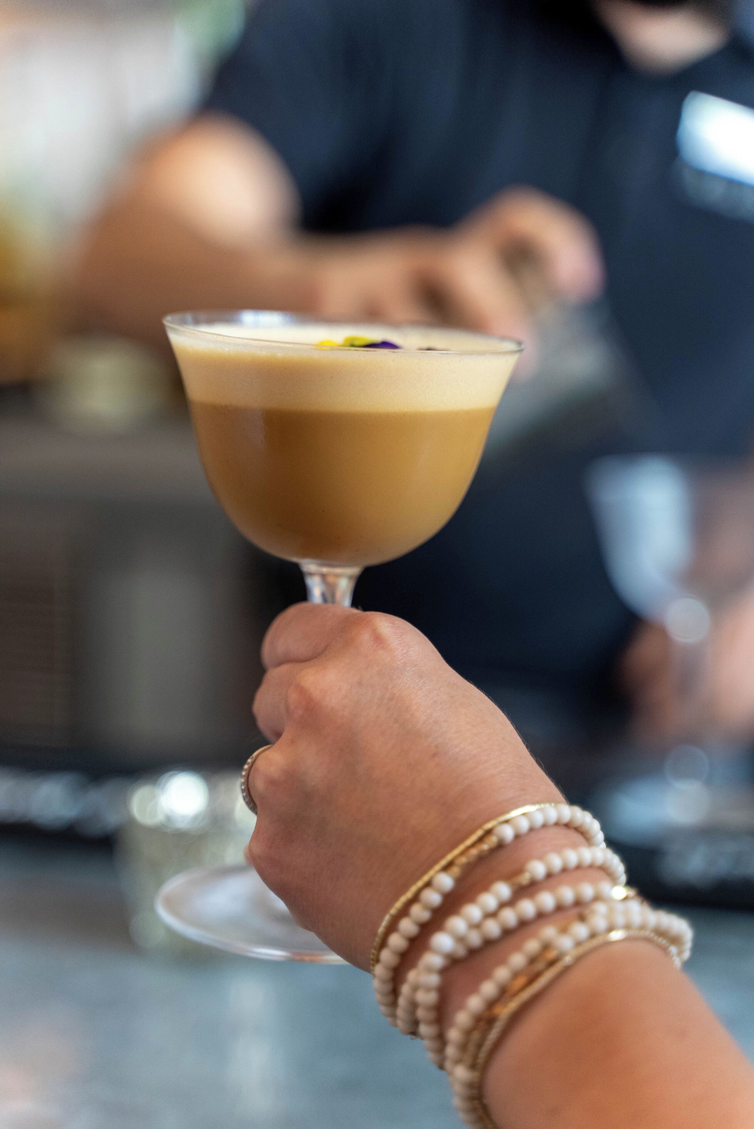 A hand holding a cocktail glass with a layered drink.