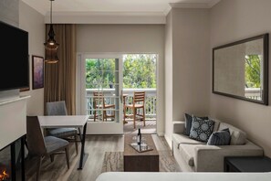 A modern living room with a sofa, a dining table, chairs, a fireplace, and a balcony with a view of trees. - River Terrace Inn (Napa)