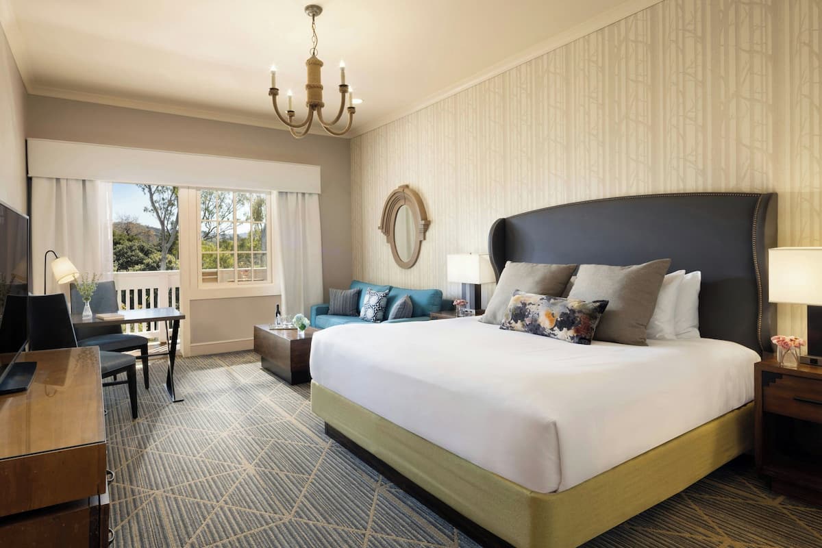 A hotel room with a large bed, a desk, a sofa, a TV, and a chandelier.
