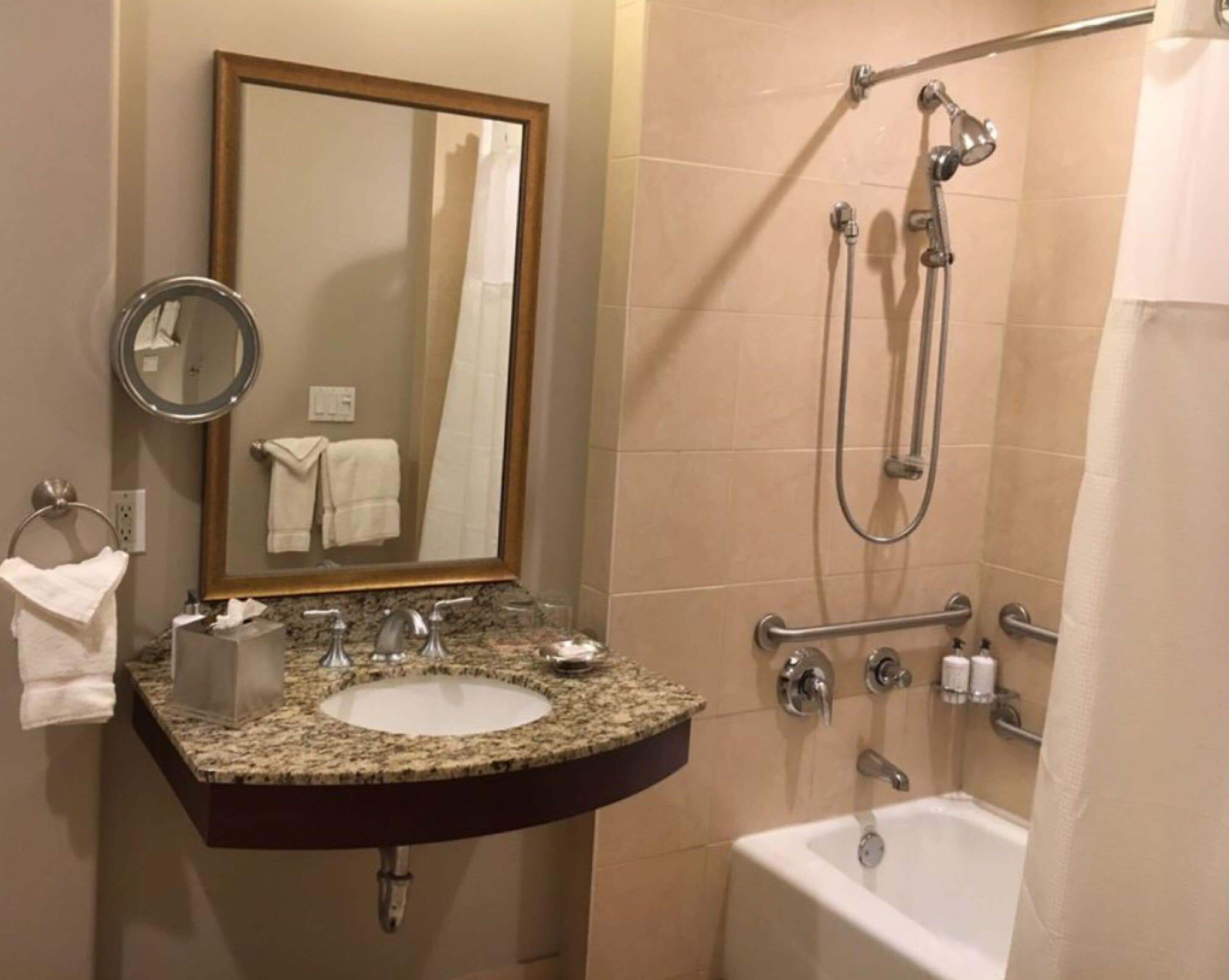 A bathroom with a granite countertop sink, a mirror, a towel rack, a shower with a handheld showerhead, and a bathtub.