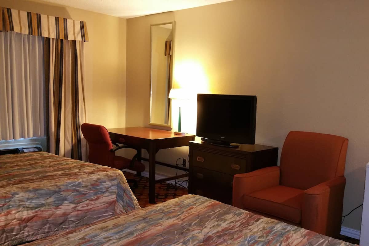 Ett hotellrum med två sängar, ett skrivbord med en tv, en stol och ett kylskåp.