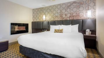 A hotel room with a large bed, a headboard with built-in lighting, a wall-mounted TV, and a patterned carpet.
