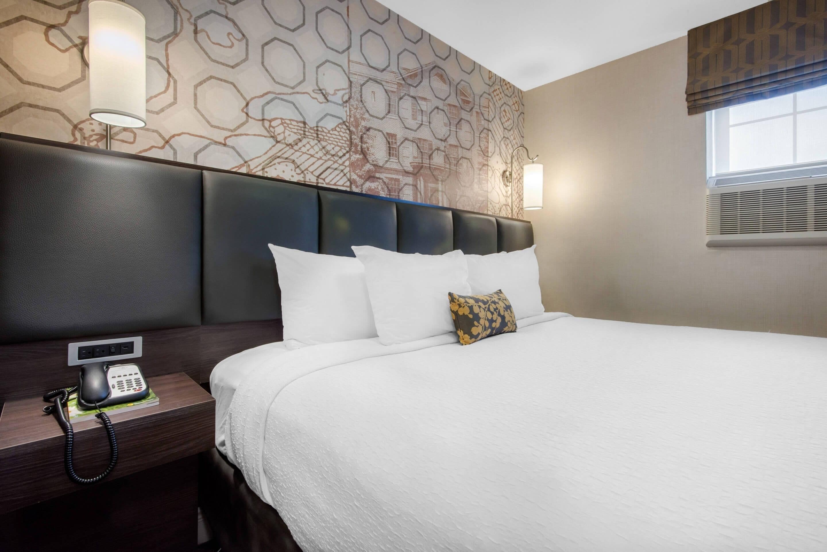Habitación de hotel con una cama grande, un teléfono en la mesita de noche y un papel tapiz estampado.