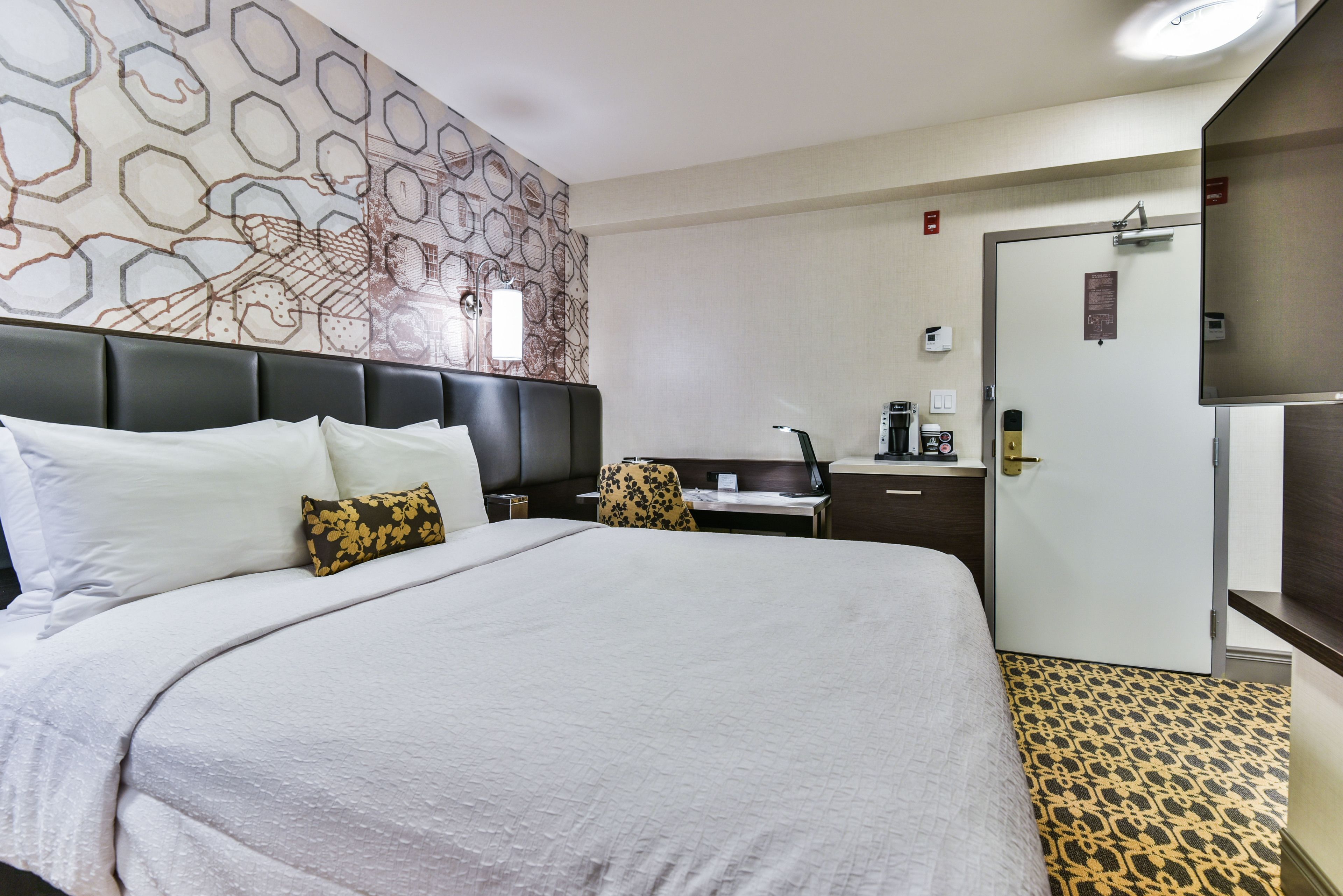 Habitación de hotel con una cama grande, un escritorio, una silla, un armario y una alfombra estampada.