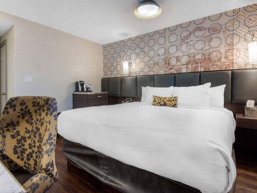 Habitación de hotel con una cama grande, una silla, una mesita de noche y una pared con diseño geométrico.