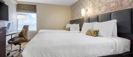 A hotel room with a large bed, a desk with a chair, a television, and a patterned carpet.