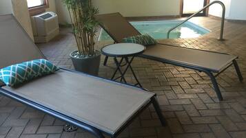 A poolside area with lounge chairs and a table, a potted plant, and a sign on the wall.