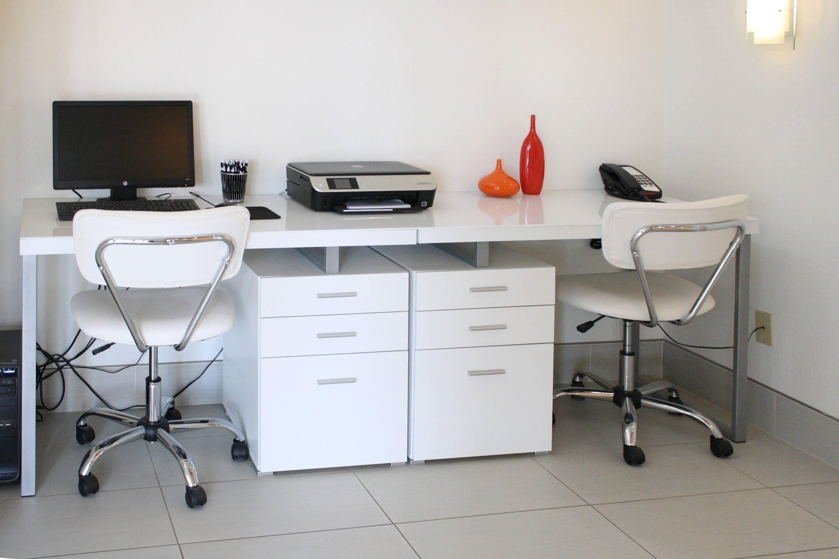 A modern office desk with a computer, printer, and office chairs.