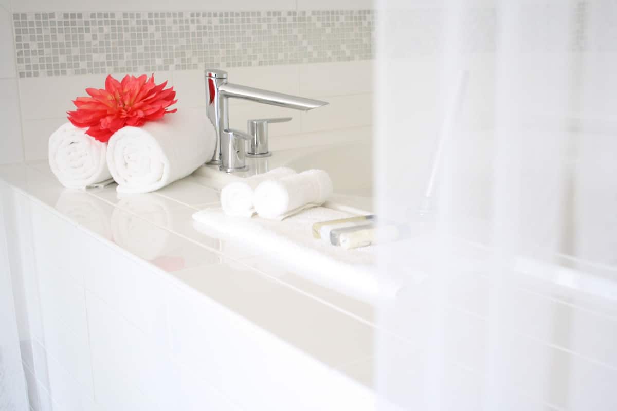 A modern bathroom with a white countertop, a chrome faucet, and neatly rolled white towels.