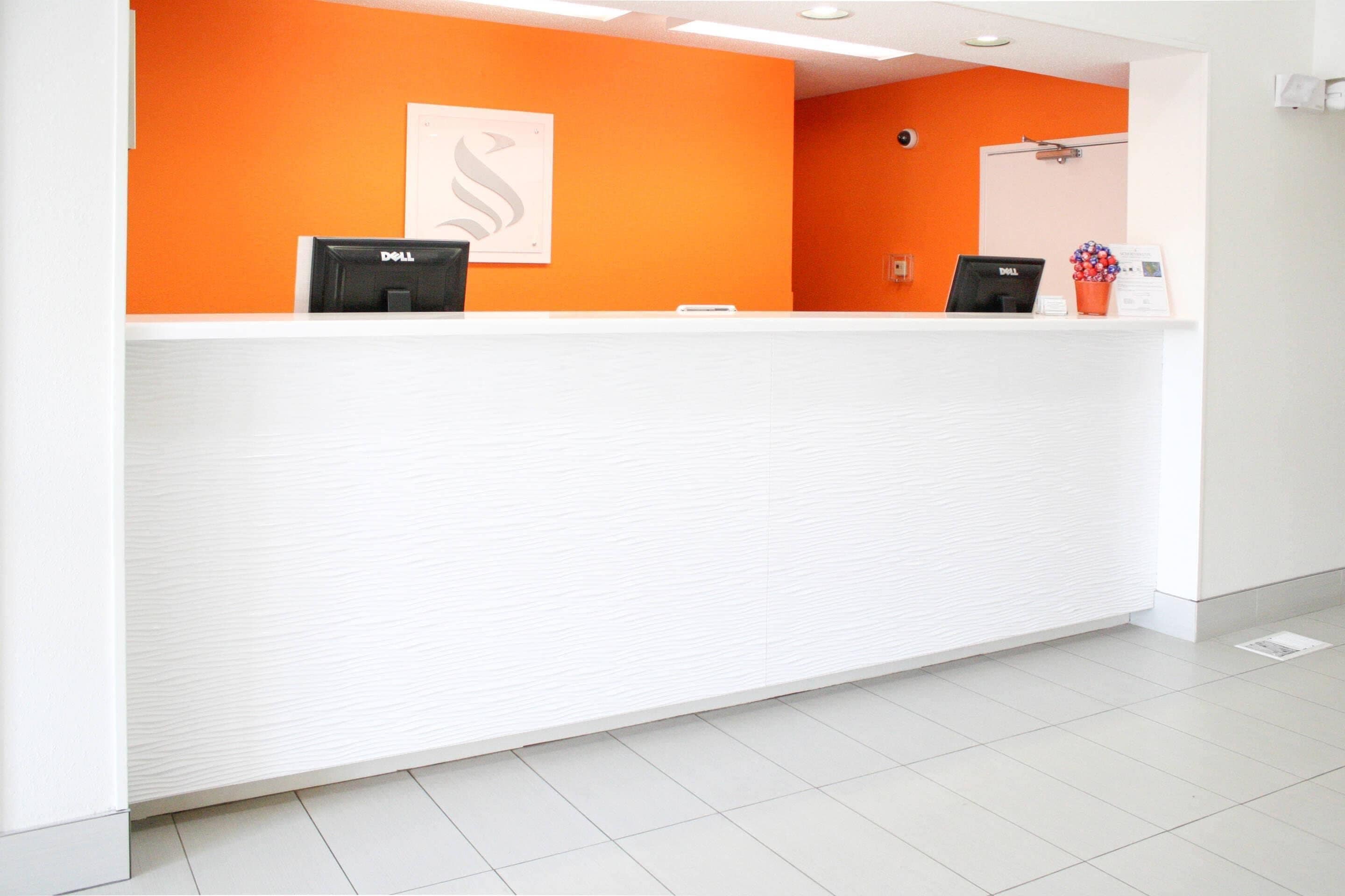 A reception desk with two monitors, a white counter, and an orange wall.