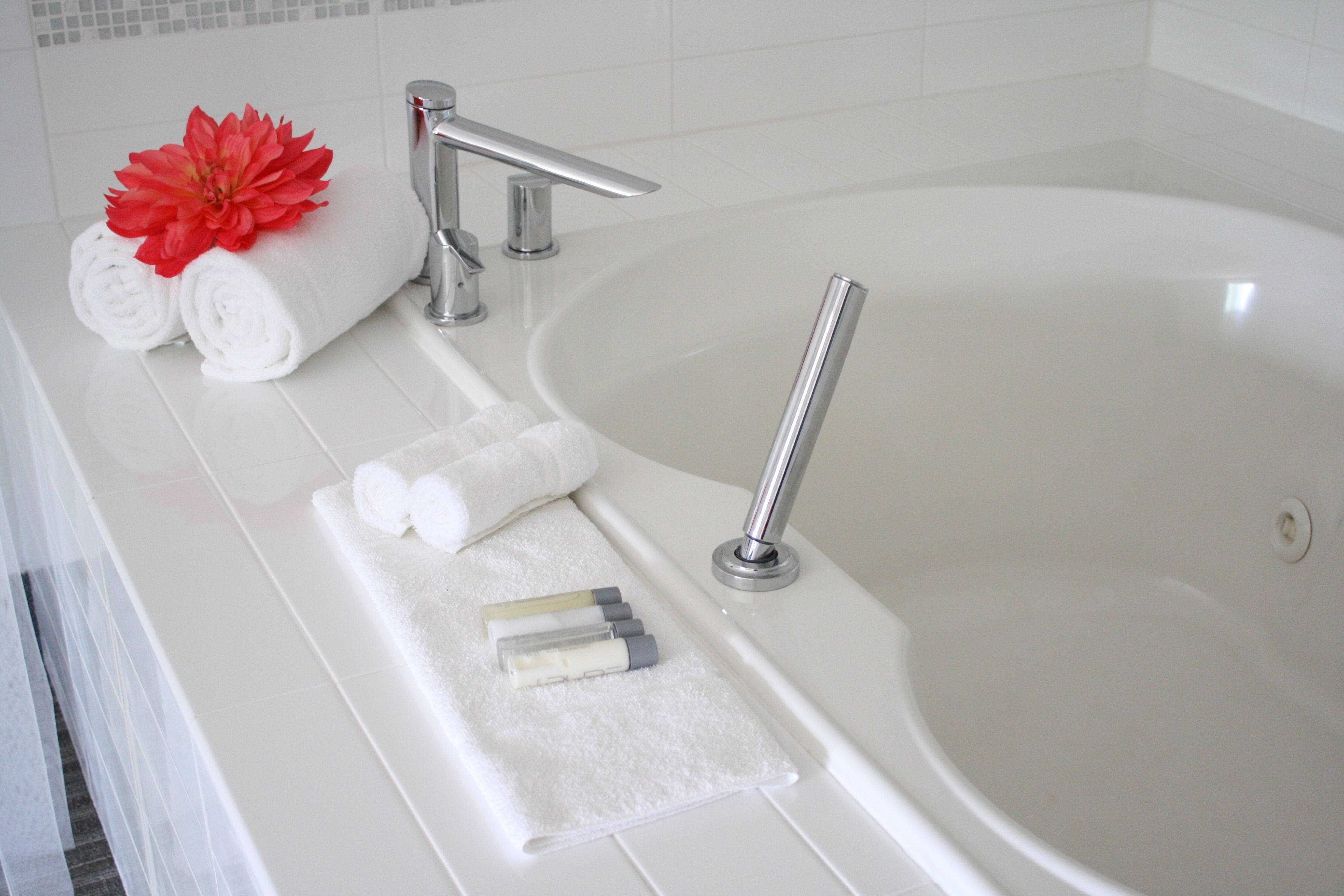 Ein Badezimmer mit einer Badewanne, zwei zusammengerollten Handtüchern, einer roten Blume und Toilettenartikeln auf einem Tablett.