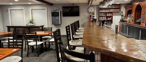 A bar area with a long counter, multiple seating arrangements, and a television mounted on the wall.