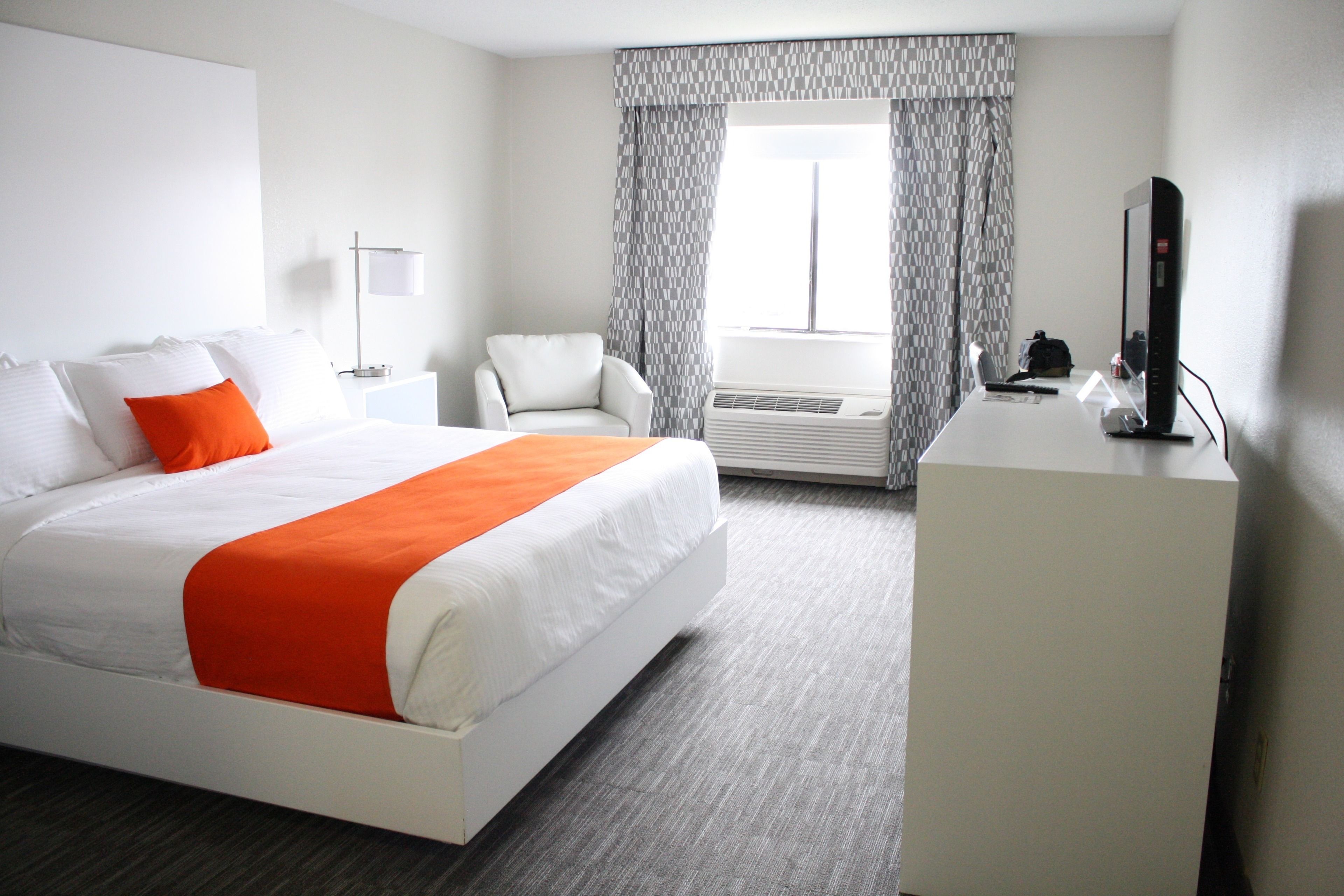 A hotel room with a large bed, a desk with a computer, a chair, and a window with curtains.