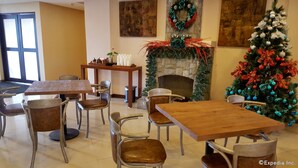 Un comedor con mesas y sillas de madera, una chimenea decorada con una guirnalda festiva, y un árbol de Navidad adornado.