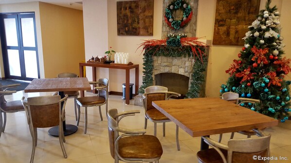 A dining area with wooden tables and chairs, a fireplace with a festive garland, and a Christmas tree with ornaments. - Microtel by Wyndham Baguio (Baguio)