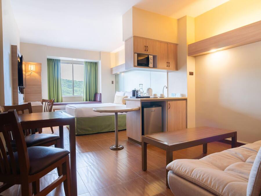 Una habitación de hotel funcional con zona de comedor, kitchenette y cama.