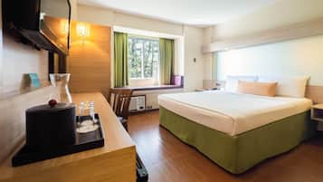 A hotel room with a bed, a desk with a lamp, a TV, and a window with curtains.