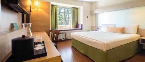 A hotel room with a bed, a desk with a lamp, a TV, and a window with curtains.