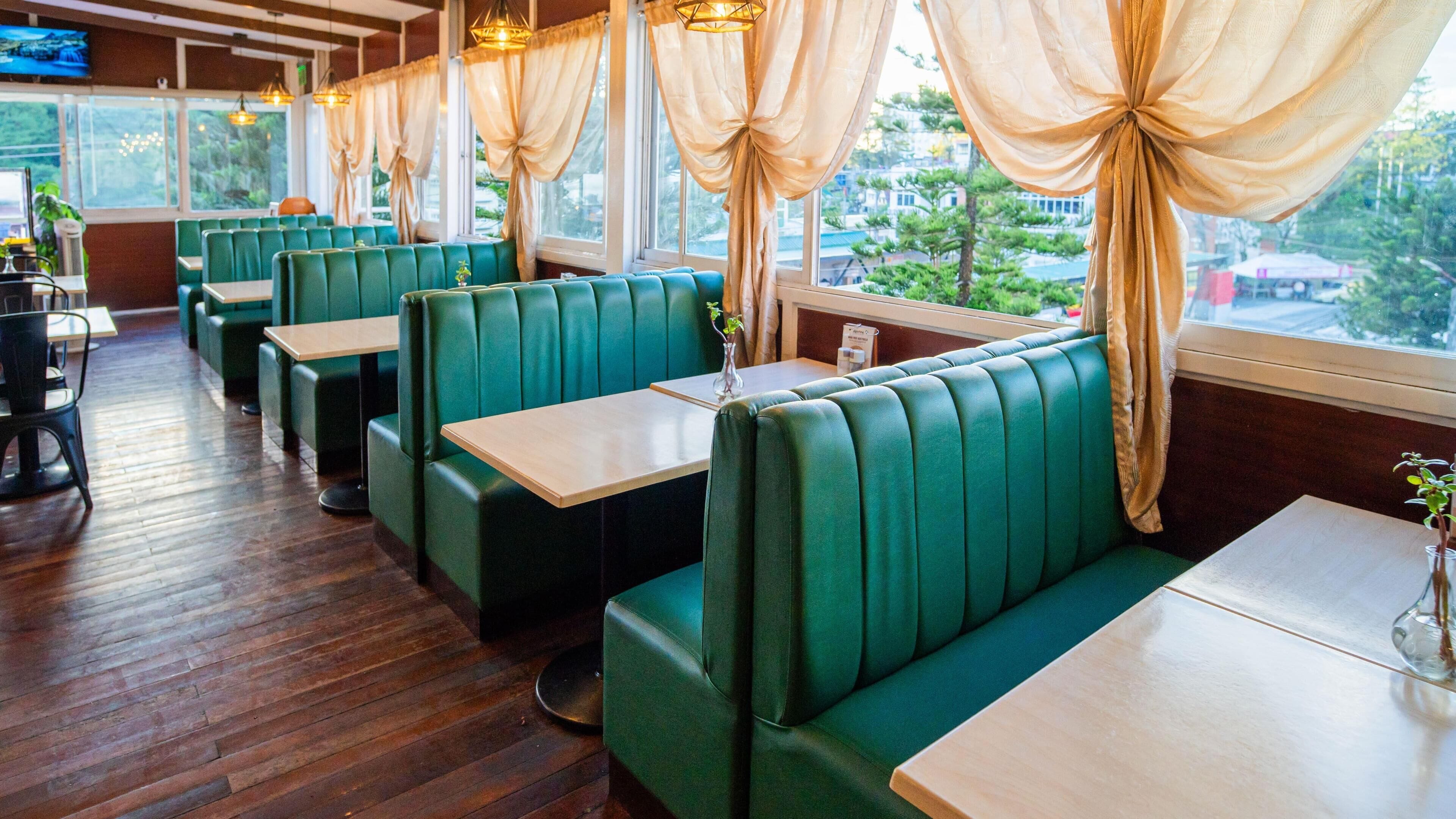 A restaurant interior with green booths, wooden tables, and large windows with curtains.