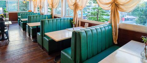 A restaurant interior with green booths, wooden tables, and large windows with curtains.