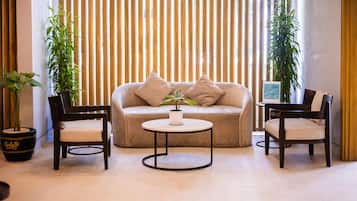 A room with a beige sofa, two wooden chairs, a small round table, and two potted plants.