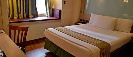 A hotel room with a bed, a desk, and a window with curtains.
