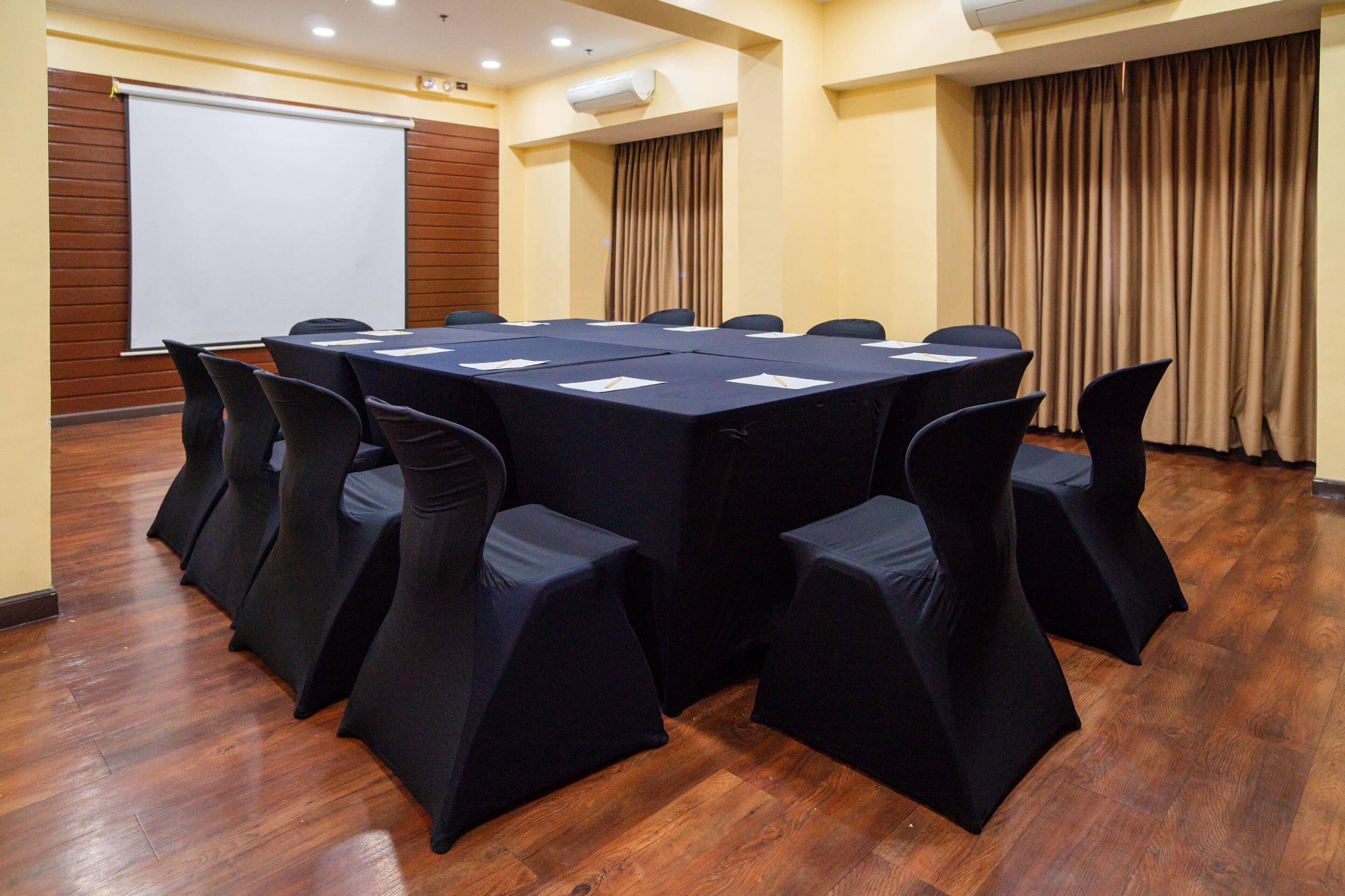 Une salle de conférence dotée d’une grande table, de chaises, d’un écran de projection et d’un plancher en bois.