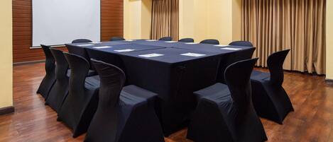 Un salón de conferencias con una gran mesa, sillas, una pantalla de proyector y piso de madera.