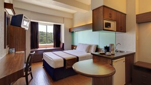 Habitación de hotel con cama, escritorio, kitchenette pequeña y ventana con cortinas.
